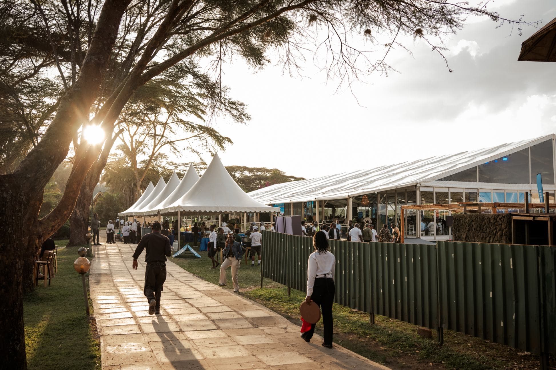 An outdoor event venue at the Carnivore Restaurant Nairobi, featuring large marquee tents, mature acacia trees and a paved walkway