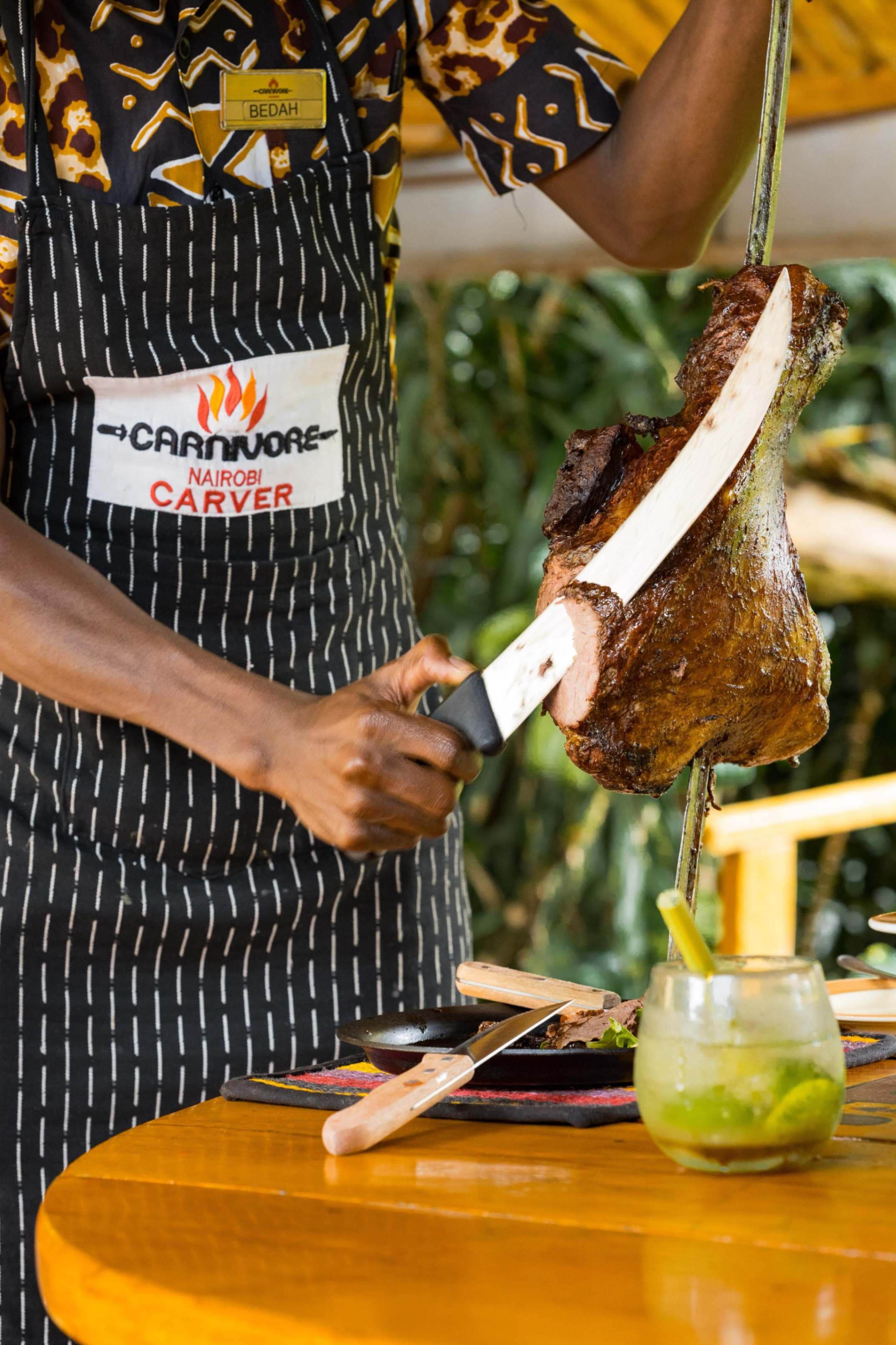 A carver in a black and white striped apron serving roasted meat from a sword at the Carnivore restaurant in Nairobi, Kenya